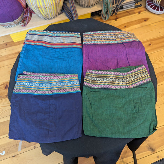 Four mridanga covers folded and displayed on a table, all varying colors of teal, dark blue, green, and magenta.